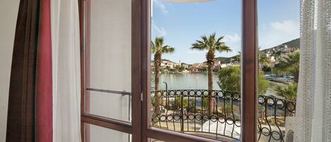 A balcony with a view of a body of water, palm trees, and a distant town.