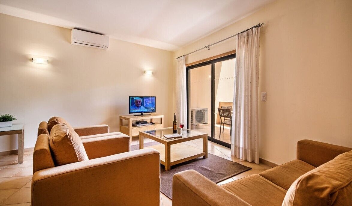 A living room with a sofa, coffee table, TV, and a sliding glass door to a balcony.