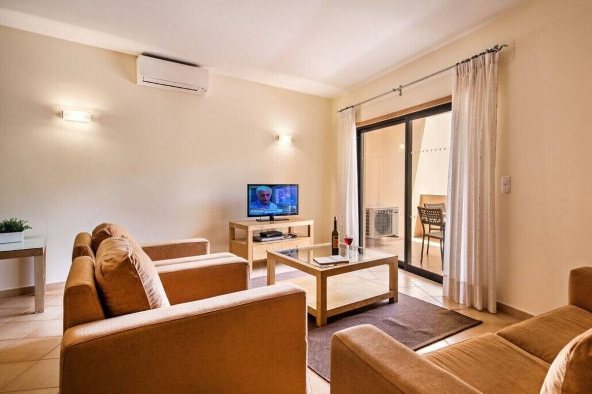 Una sala de estar con sofá, mesa de centro, televisor y puerta corrediza de vidrio a un balcón.