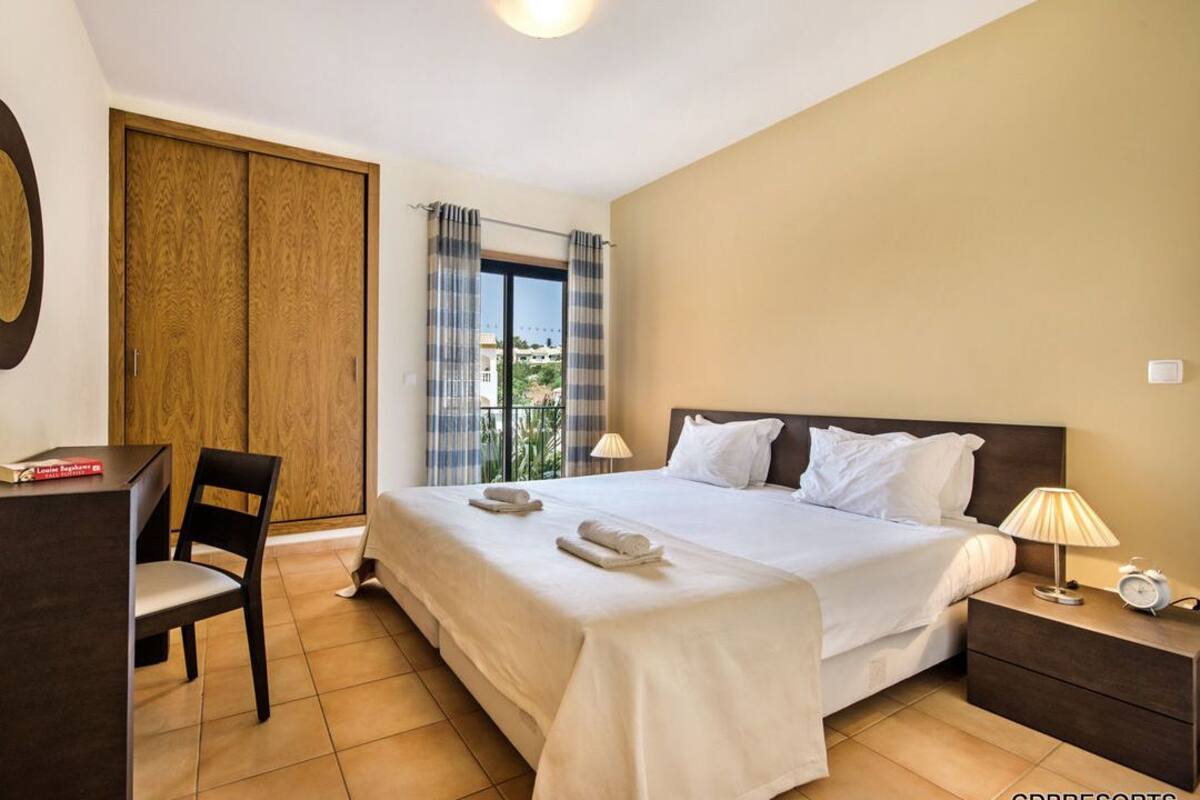 Habitación de hotel con cama, escritorio, silla, armario y ventana con cortinas.