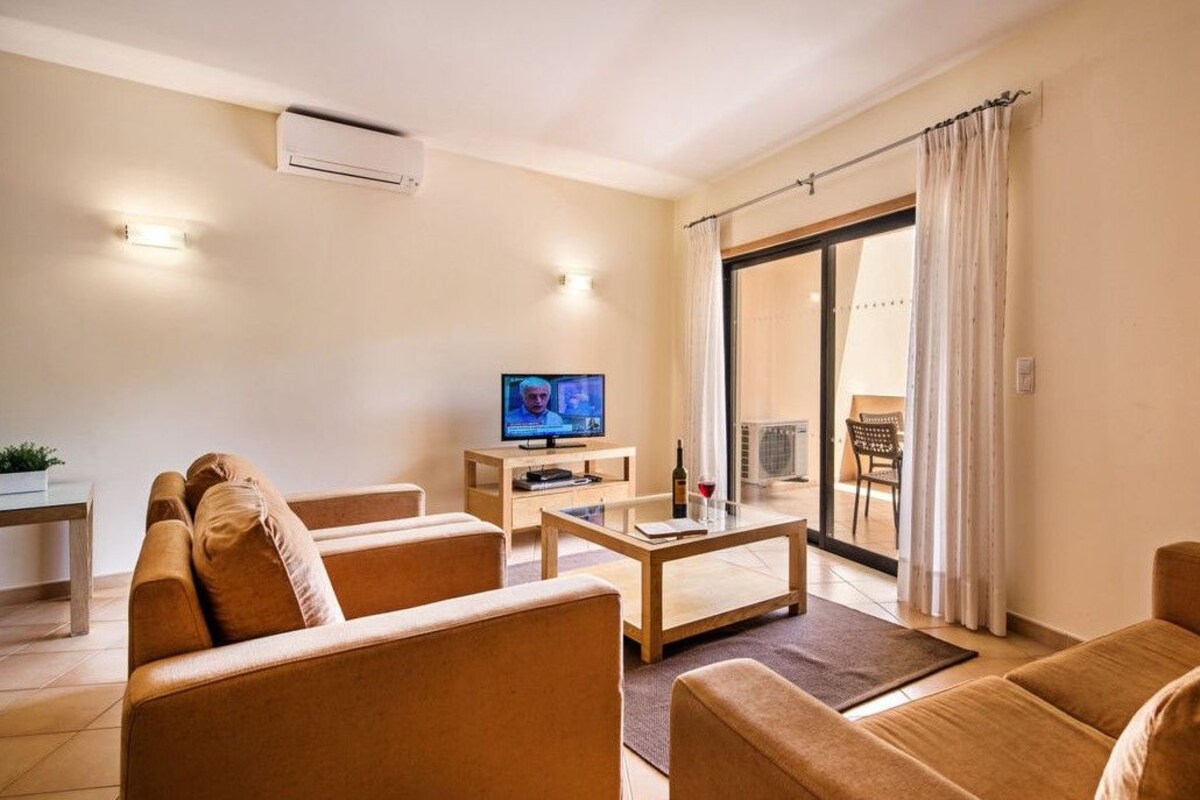 A living room with a sofa, coffee table, TV, and a sliding glass door to a balcony.