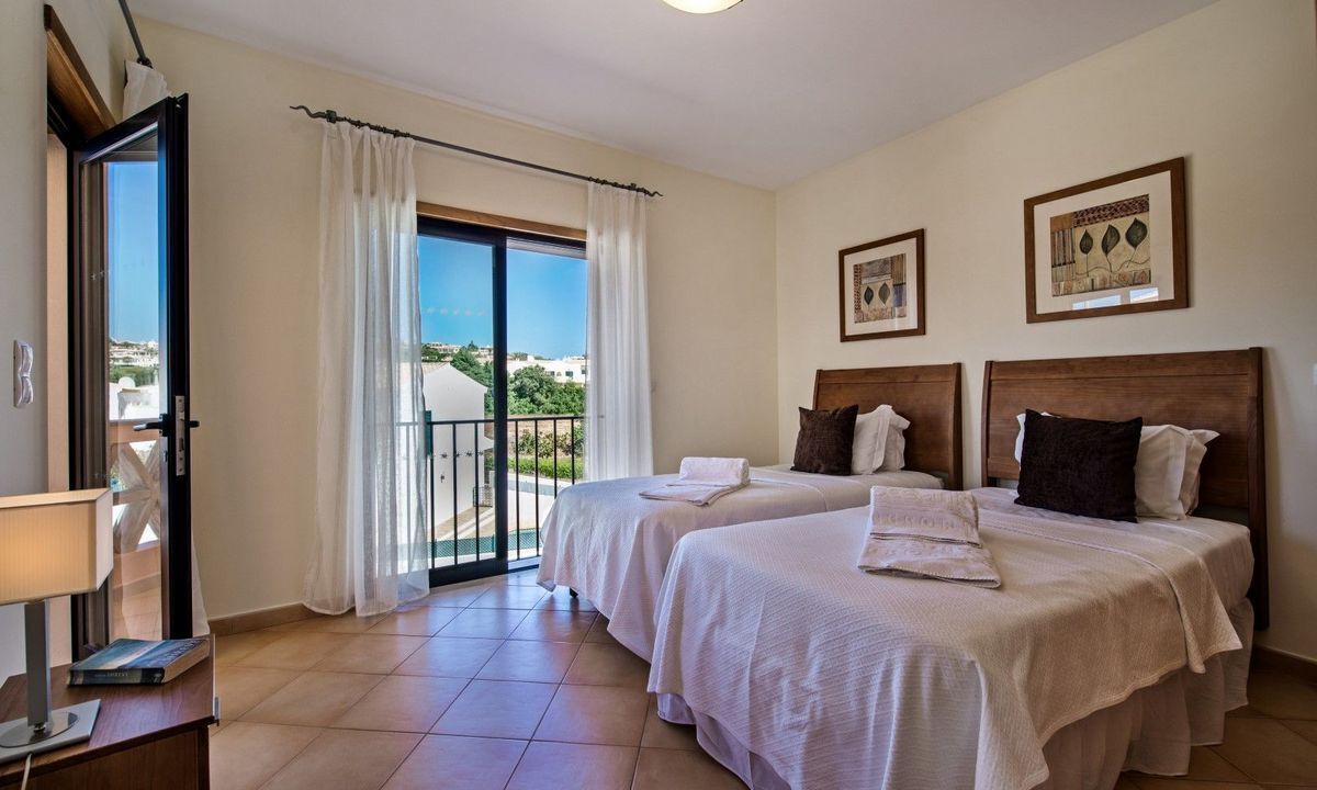 A hotel room with two beds, a balcony with a view, and a desk with a lamp.