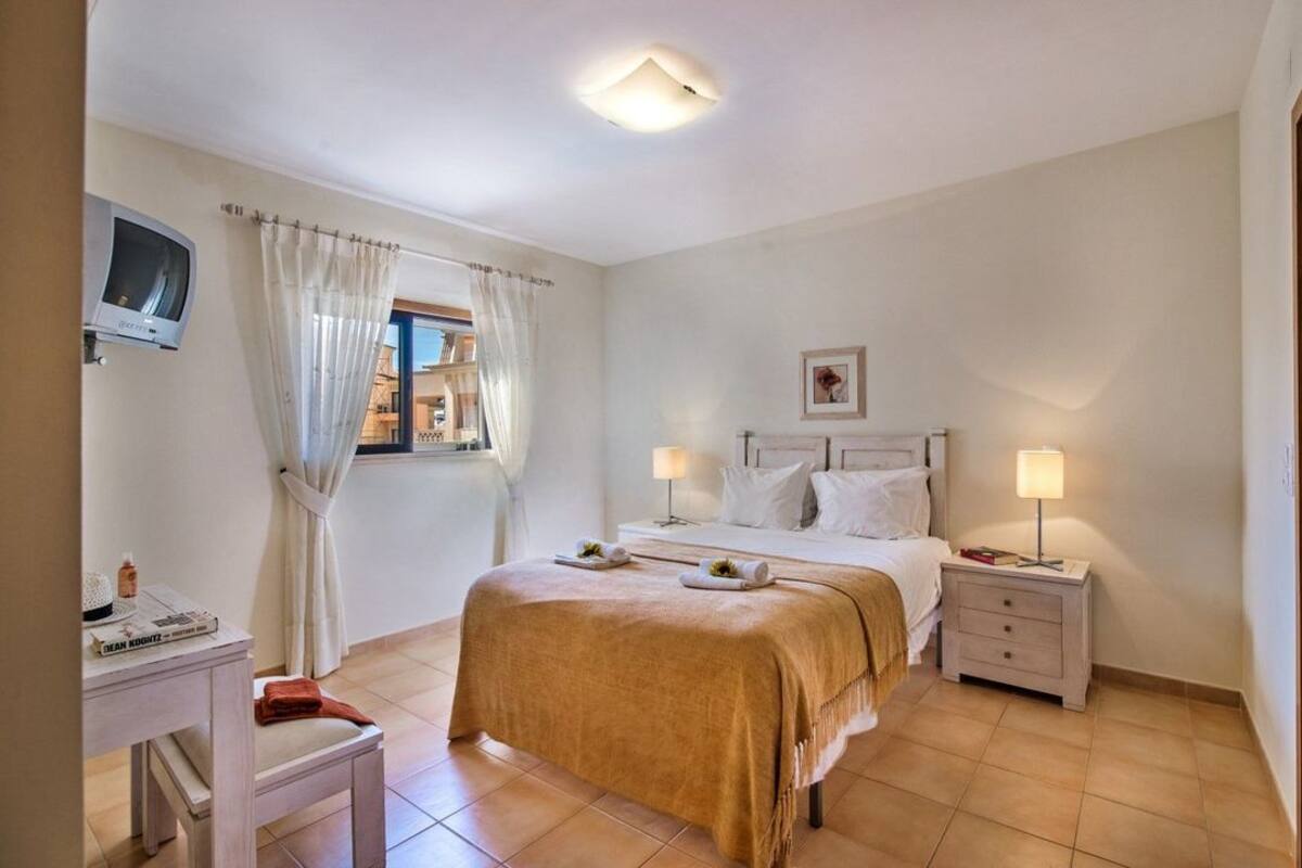 Un dormitorio con una cama, dos mesitas de noche, un escritorio, una silla y un televisor.