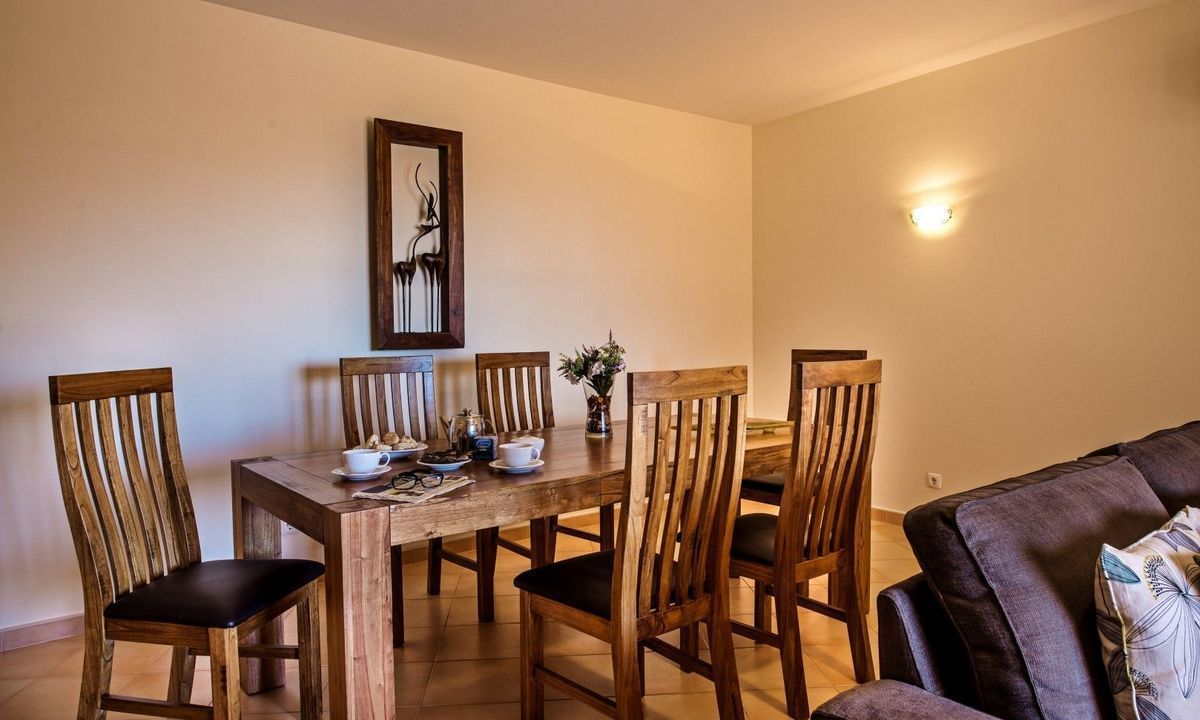 A dining area with a wooden table and chairs, a vase with flowers, and a framed artwork on the wall.
