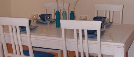 A dining area with a white table and chairs, blue cushions, and a painting on the wall.