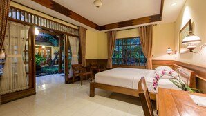 A hotel room with a bed, wooden furniture, a window with a view of greenery, and a ceiling fan. - Duta Garden Hotel (Yogyakarta)