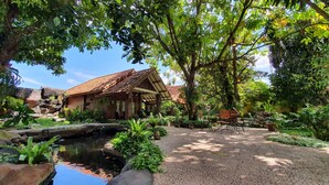 A rustic building with a tiled roof, surrounded by lush greenery and a small pond. - Duta Garden Hotel (Yogyakarta)