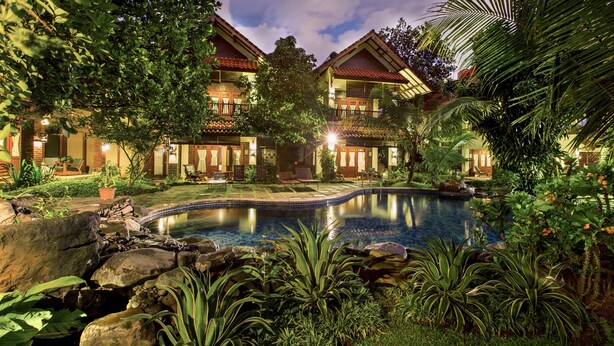 A resort with a swimming pool, lush greenery, and a well-lit building with multiple balconies. - Duta Garden Hotel (Yogyakarta)