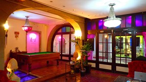 A billiards room with a pool table, a red armchair, and a potted plant.