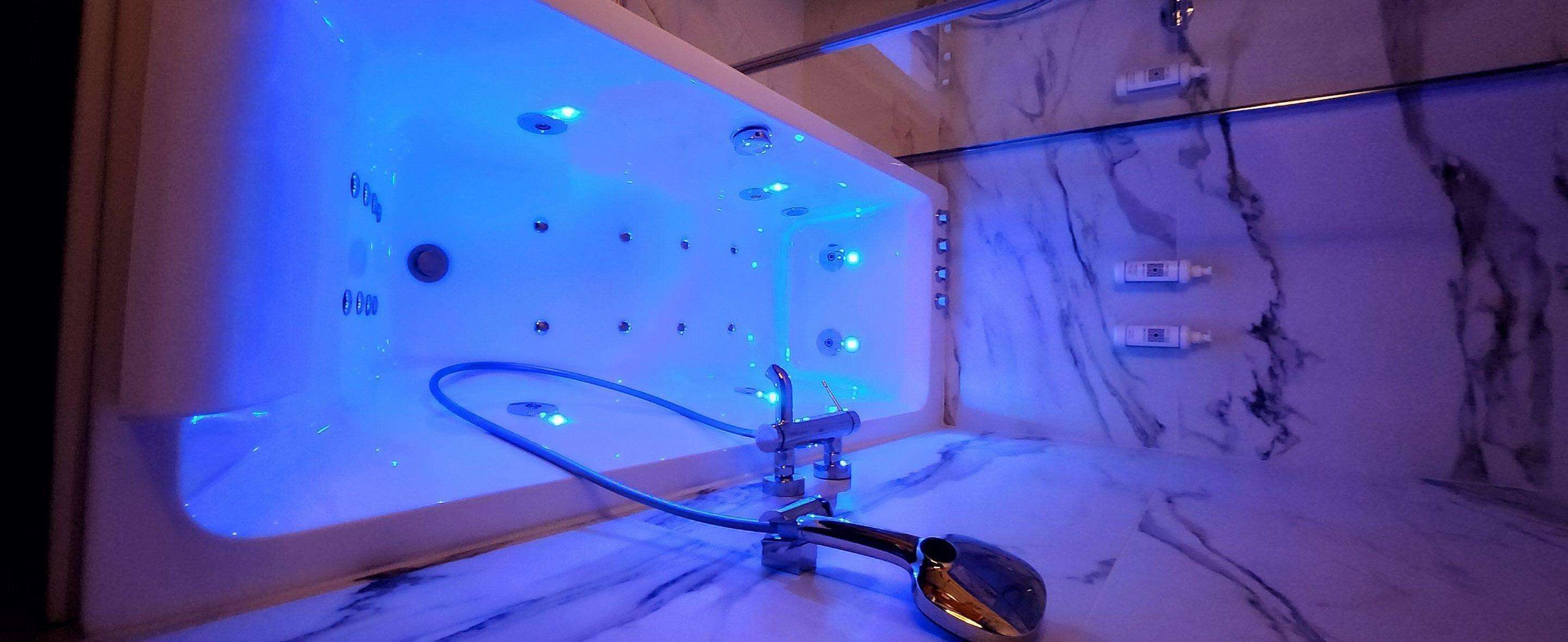 Ein Badezimmer mit Marmorboden, einer Badewanne mit blauer LED-Beleuchtung und einer Handbrause.