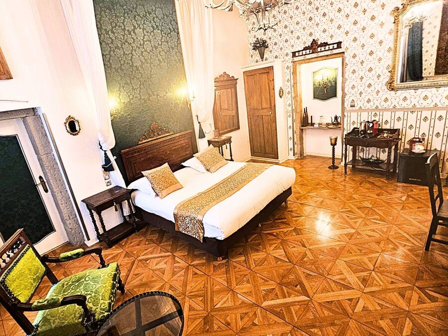 Quarto com uma cama grande, um candelabro, papel de parede estampado e piso de madeira.