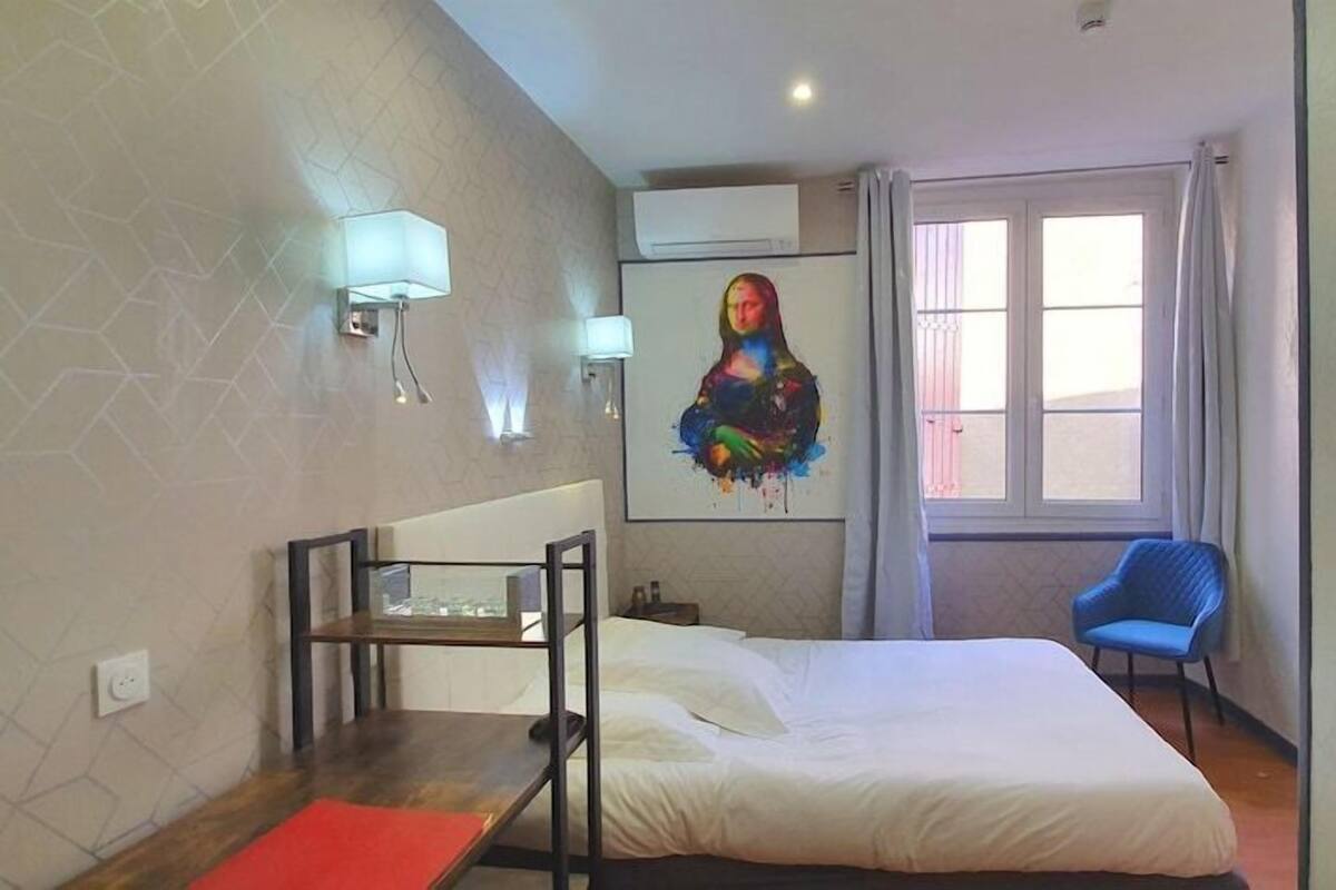 A hotel room with a bed, a desk, a chair, and a large window.