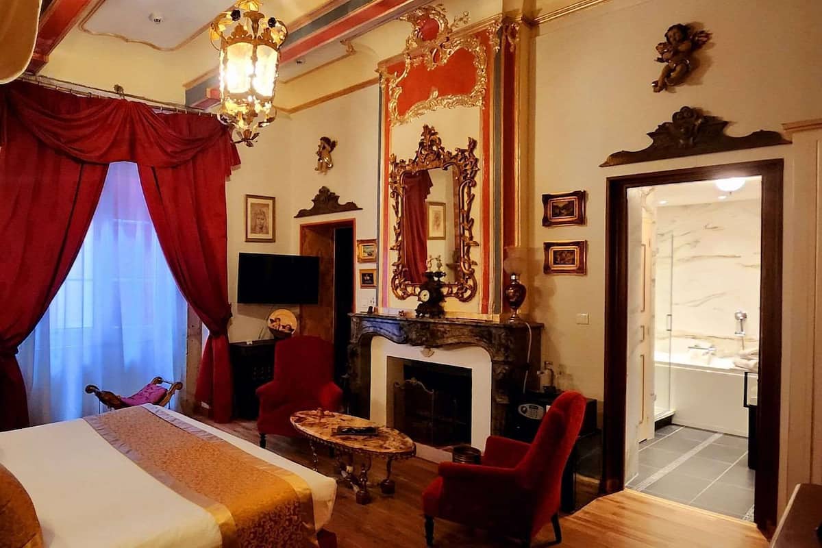 A hotel room with a bed, a fireplace, a TV, and a red chair.