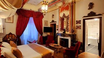 Une chambre d’hôtel avec un lit, une cheminée, une télévision et un fauteuil rouge.