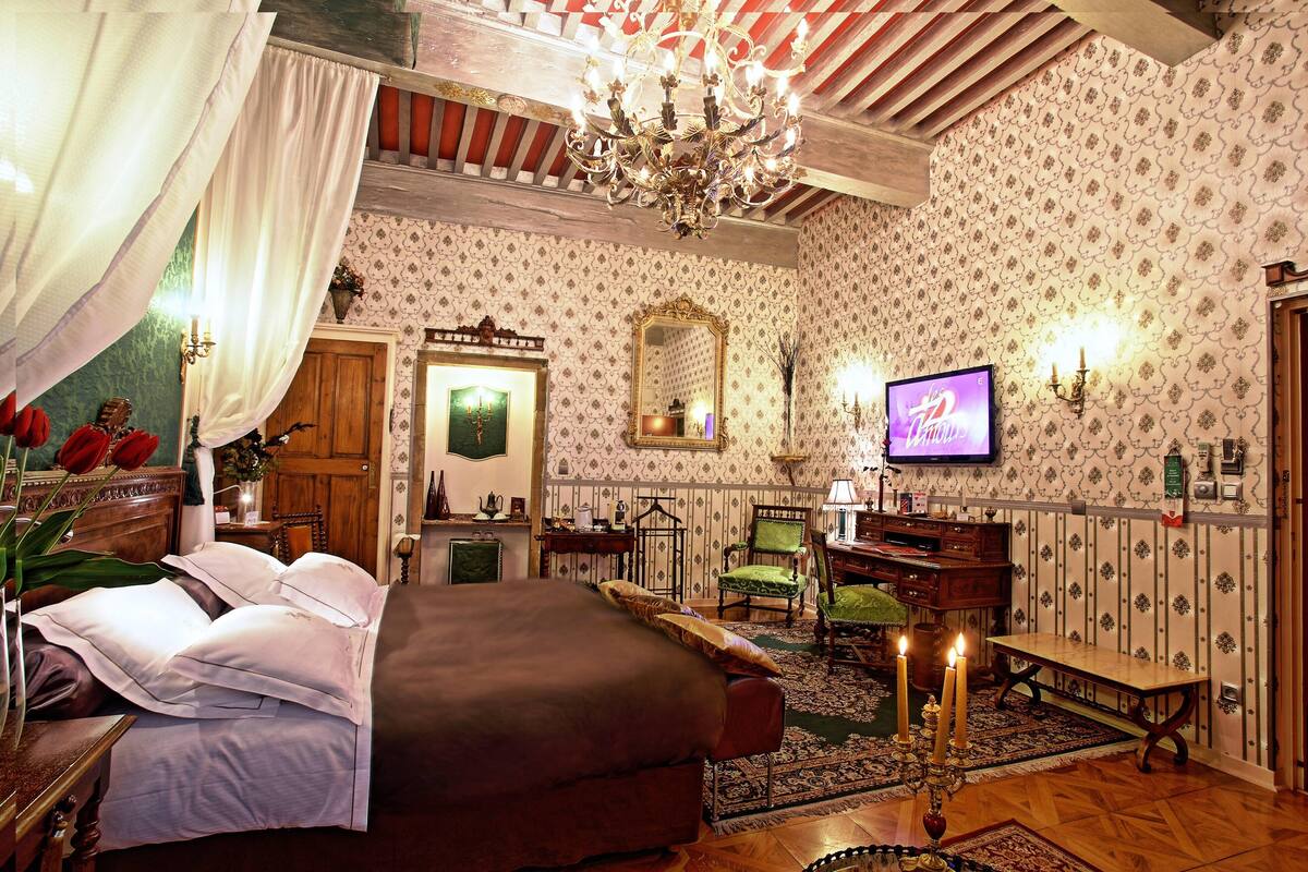 A room with a bed, a television, a chandelier, and a patterned wallpaper.