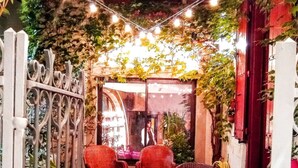 An outdoor seating area with wicker furniture and a small table, surrounded by a decorative fence and string lights.