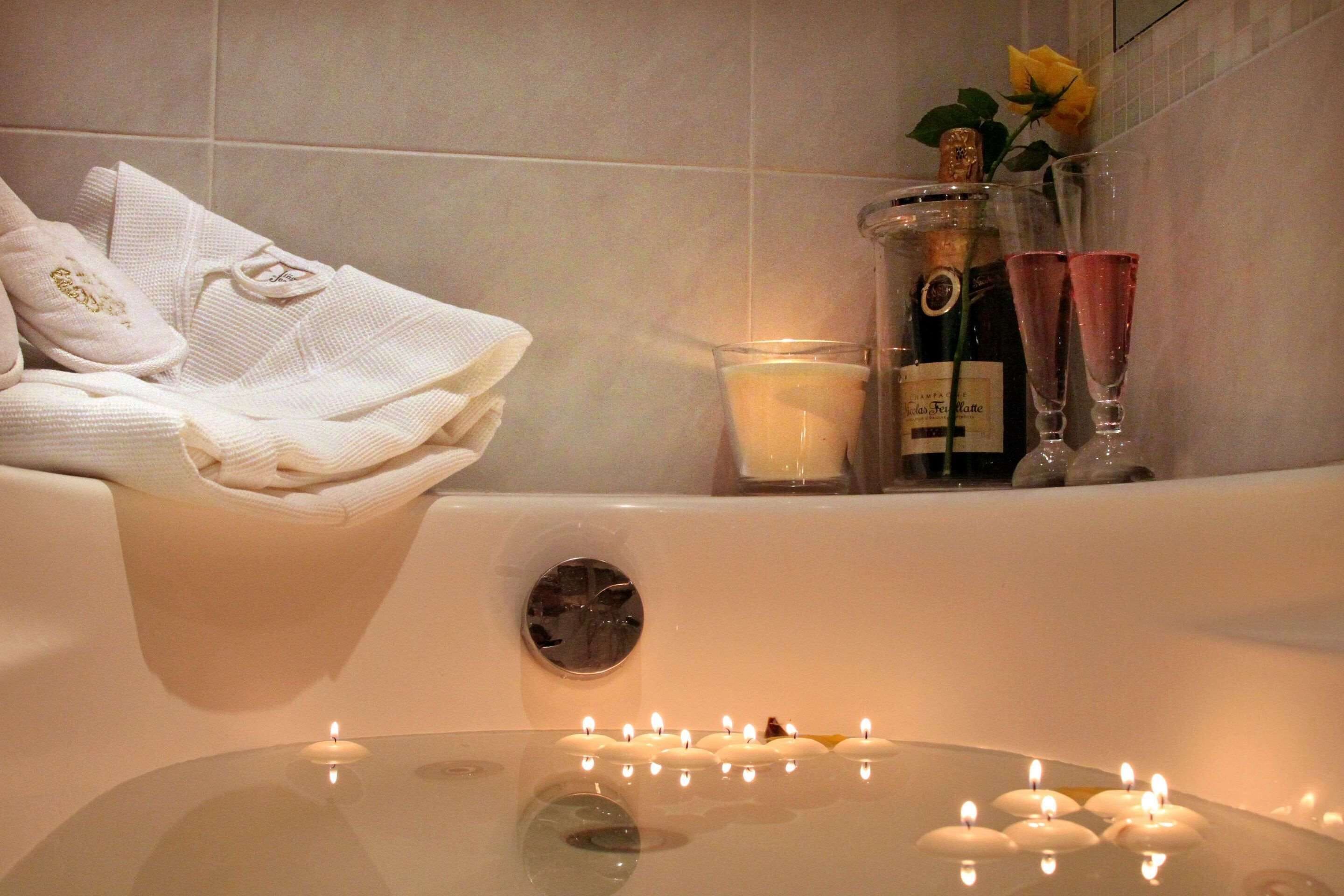 A bathtub with candles, a bottle of perfume, and a glass of champagne.
