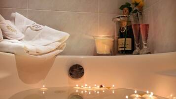 A bathtub with candles, a bottle of perfume, and a glass of champagne.