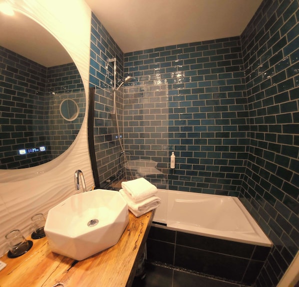 A bathroom with a white sink, a wooden vanity, a white bathtub, and blue-tiled walls.