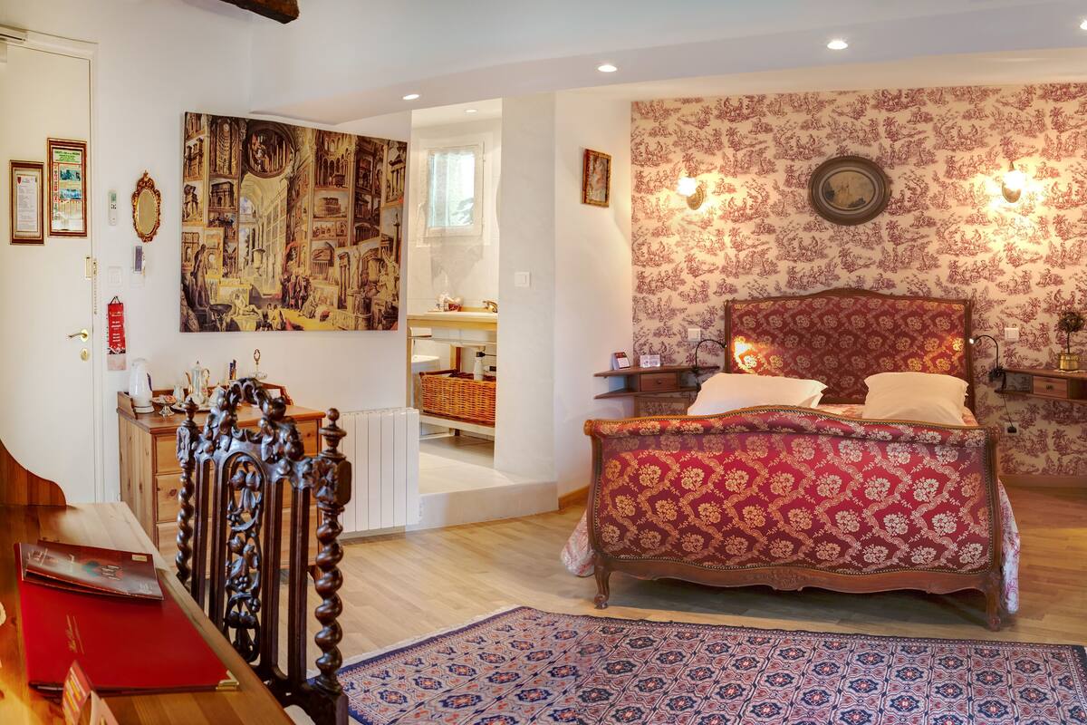 A bedroom with a large bed, a wooden dresser, a desk with a computer, and a chair.