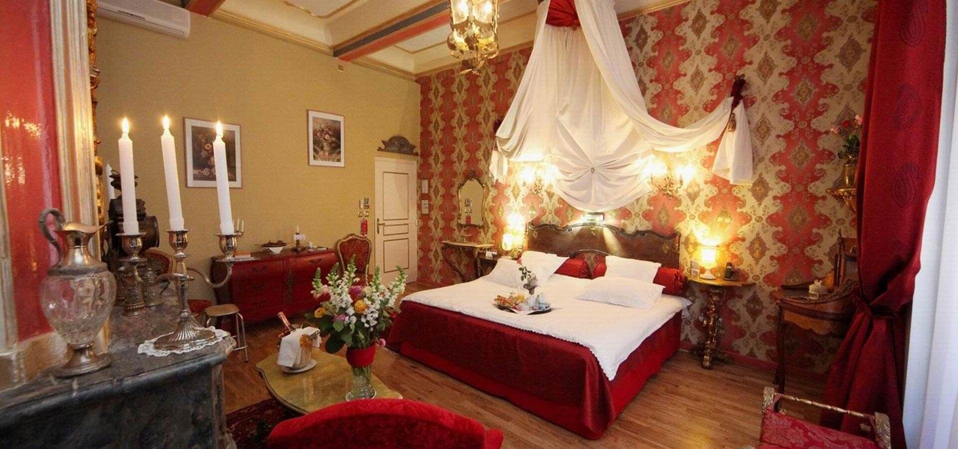 Un dormitorio con una cama grande, una mesita de noche, un aparador y un espejo. Hay velas sobre el aparador y un florero sobre la mesita de noche.