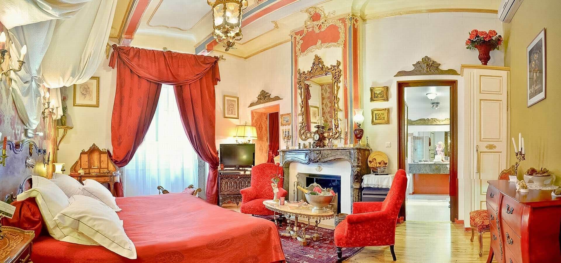 A room with a large bed, a fireplace, a red armchair, and a mirror.
