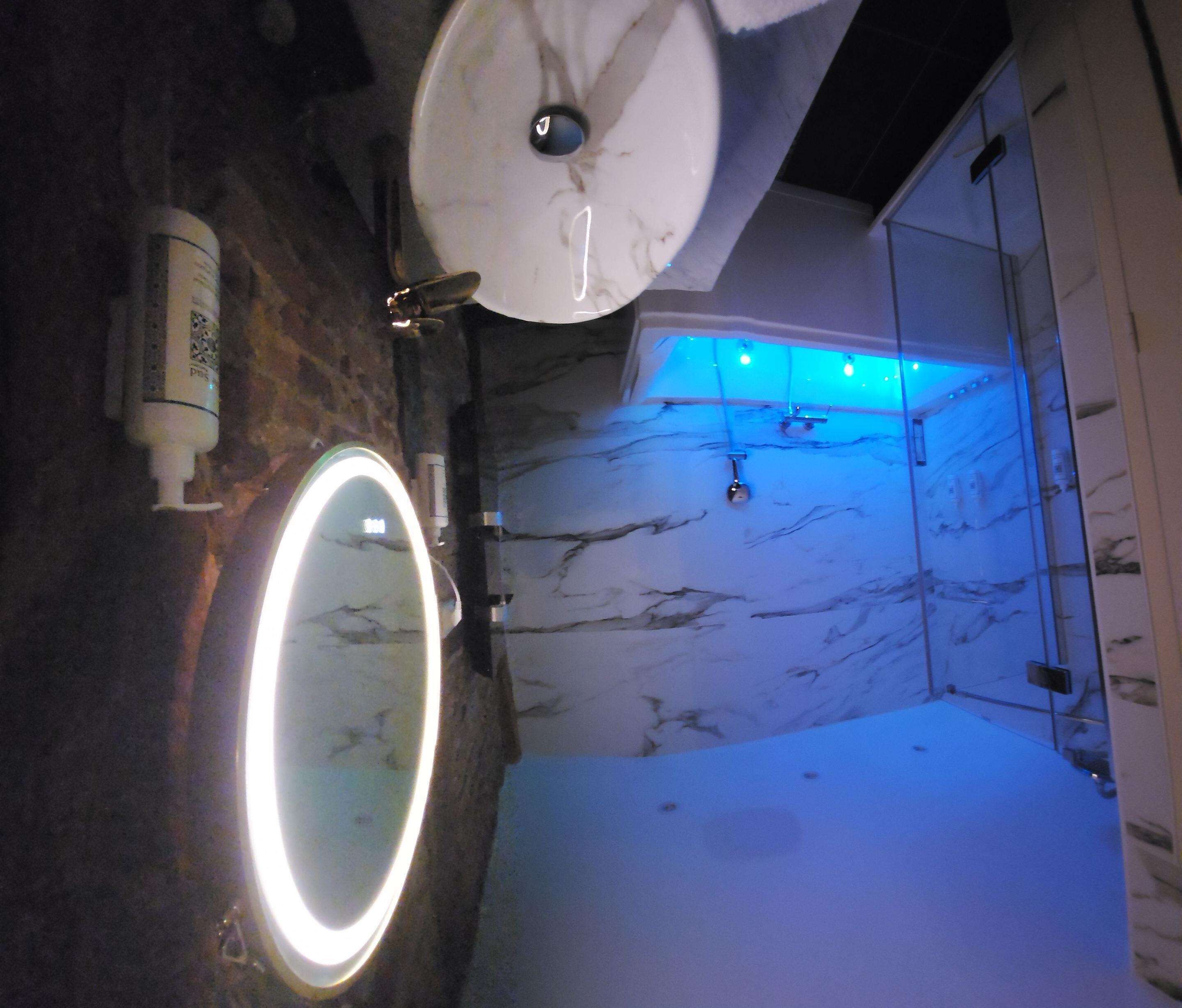 Un baño con pared de mármol, un lavabo con espejo y zona de ducha.