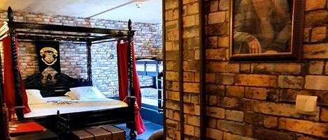 A room with a brick wall, a bed with a canopy, a desk, and a chair.