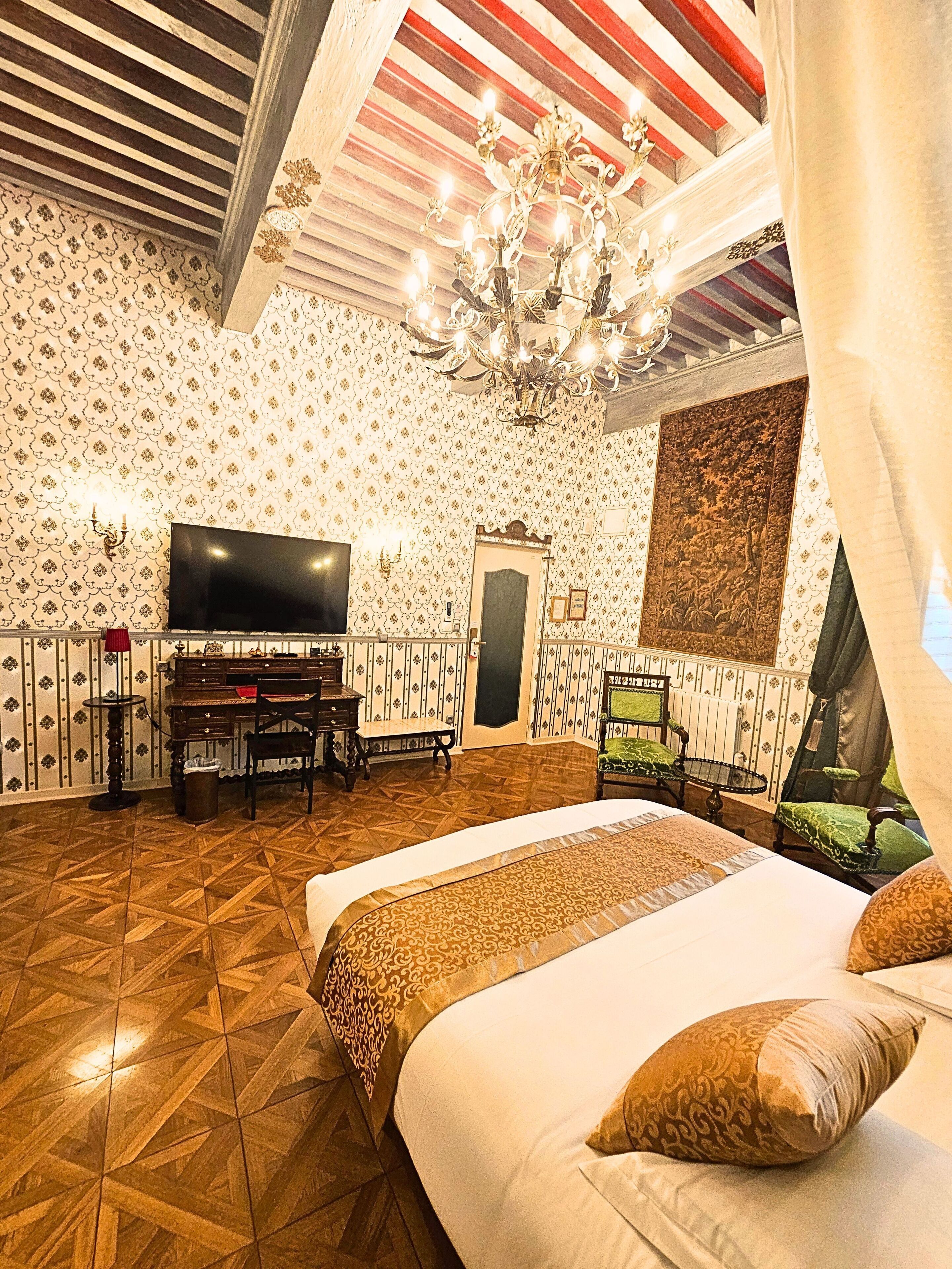 Una camera da letto con un grande letto, una televisione, un pianoforte e un lampadario.
