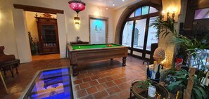 A billiards room with a pool table, a billiard cue rack, and a glass table.