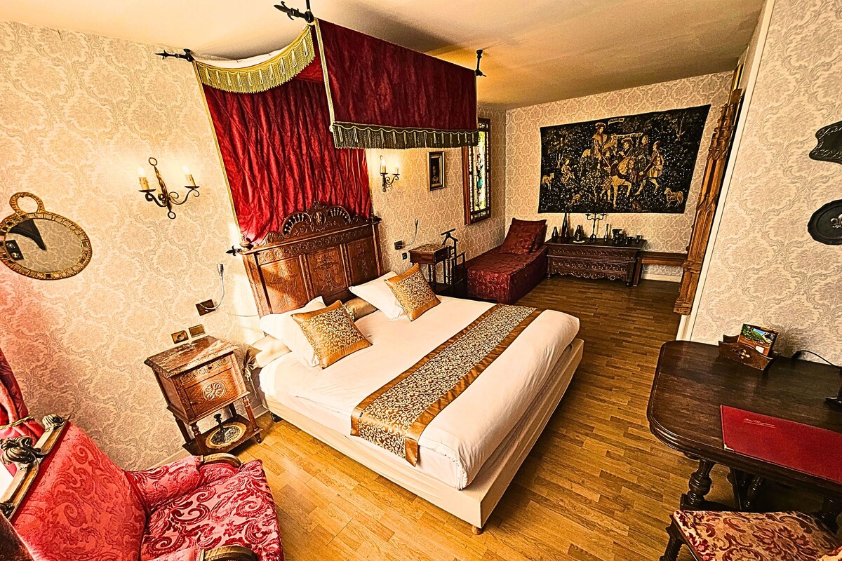 A room with a large bed, a wooden headboard, a red chair, a small table, and a painting on the wall.