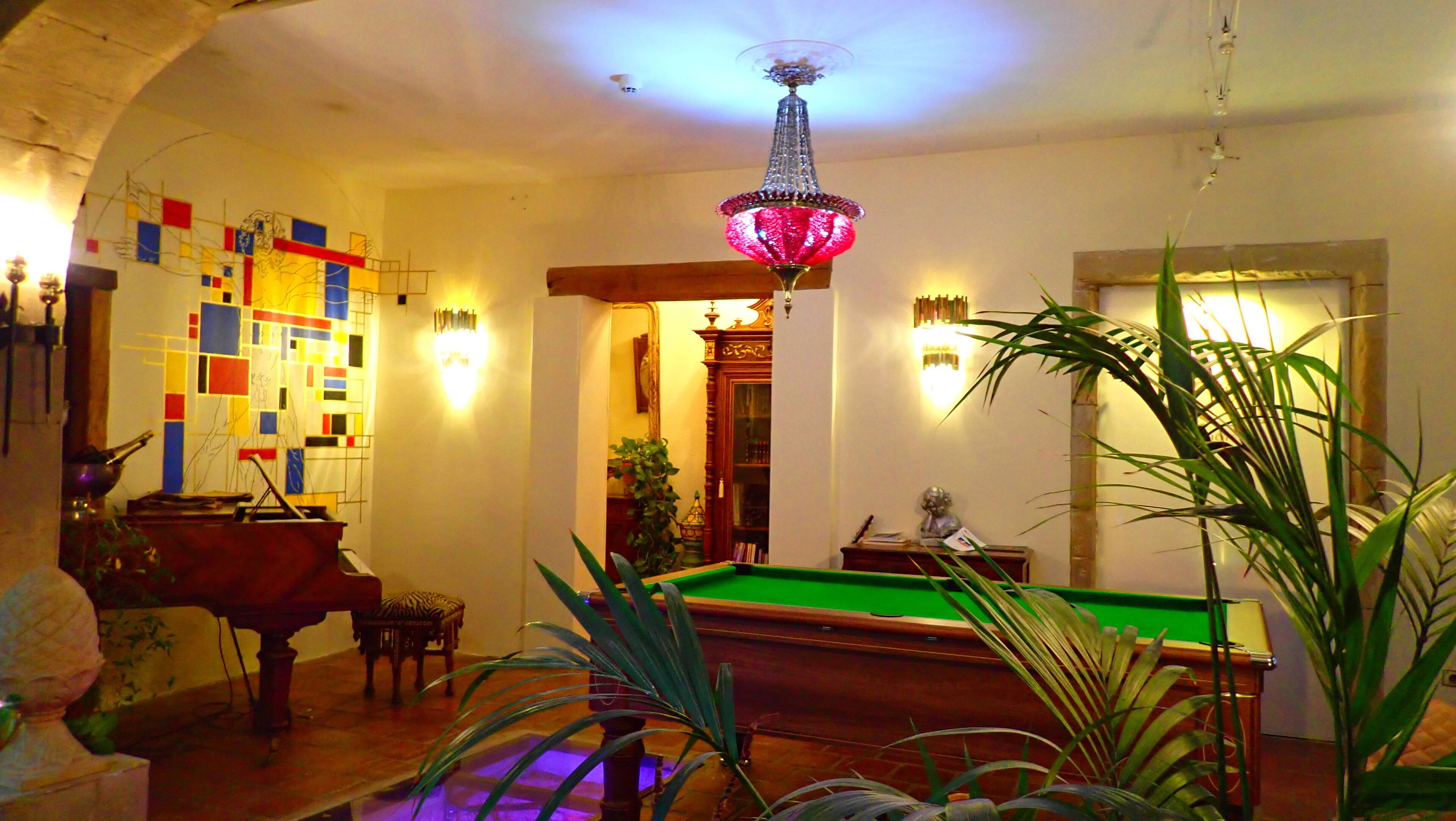 Una sala de billar con mesa de pool, un piano y una pared decorativa con diseños geométricos.