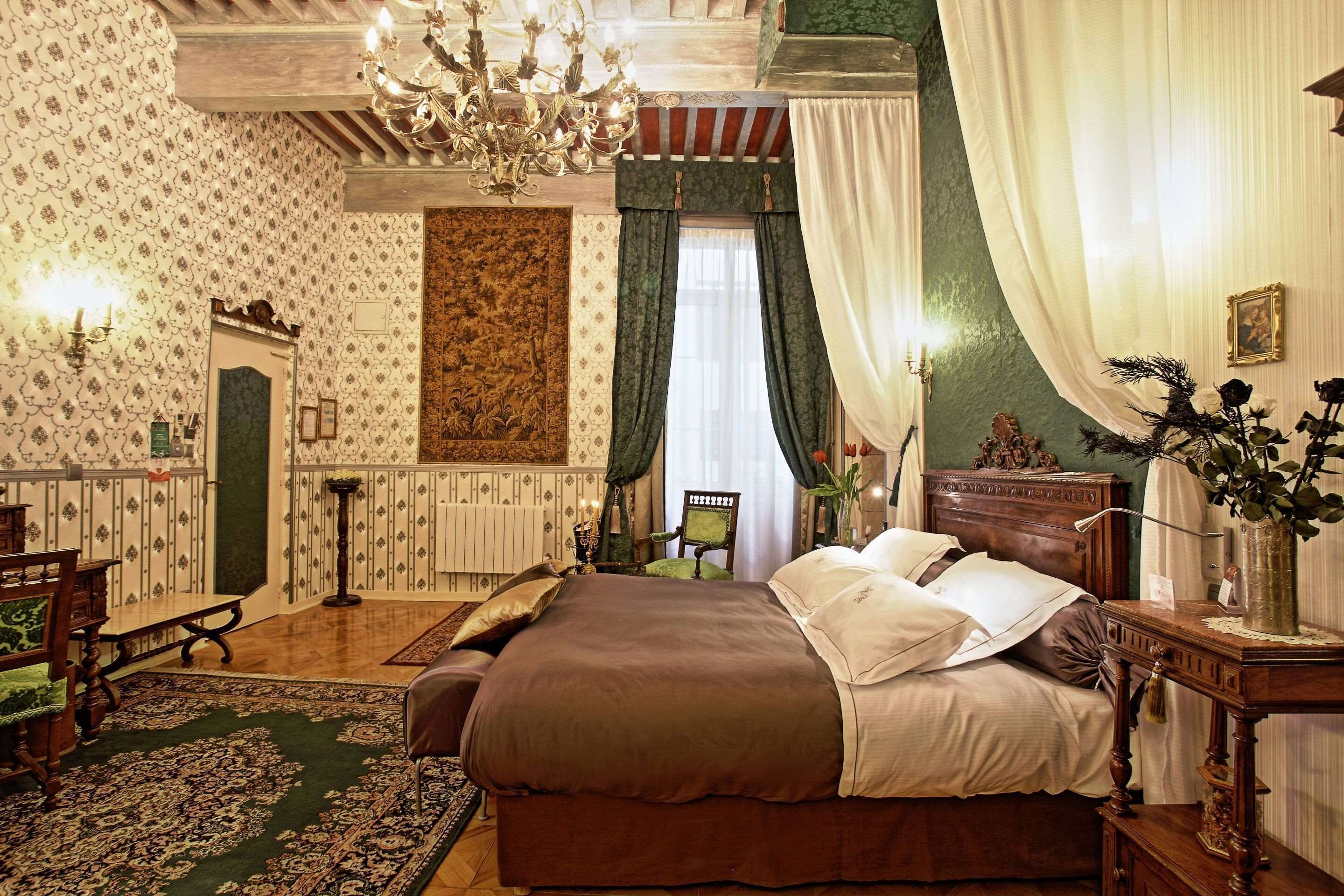 Un dormitorio tradicional con una cama grande, una araña, una pared de acento verde y una chimenea.