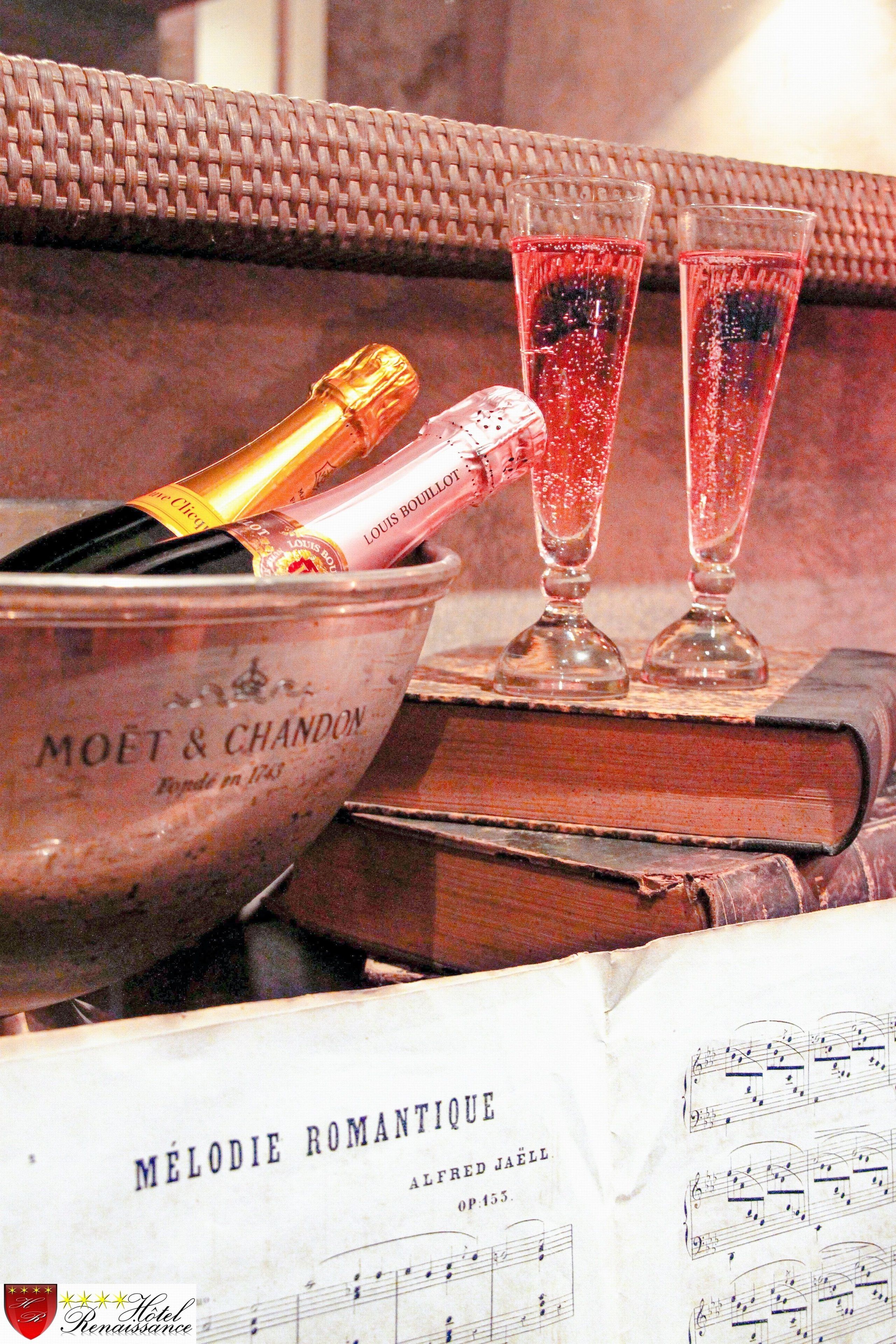A bucket labeled "MOET & CHANDON" with champagne bottles and glasses, placed on a table with a book and sheet music titled "MÉLODIE ROMANTIQUE" by Alfred Jaell.