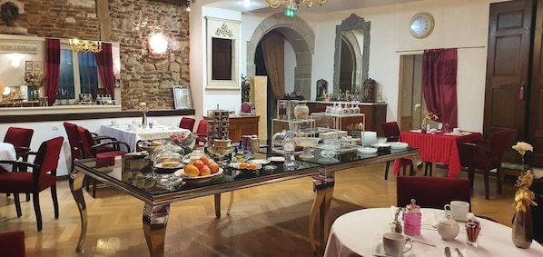A dining area with tables set for breakfast, including fruits and pastries.