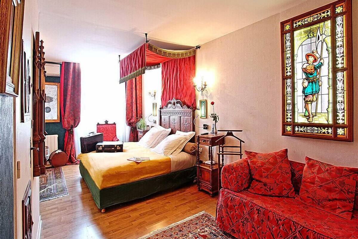 A bedroom with a bed, a red sofa, a wooden dresser, and a stained glass window.