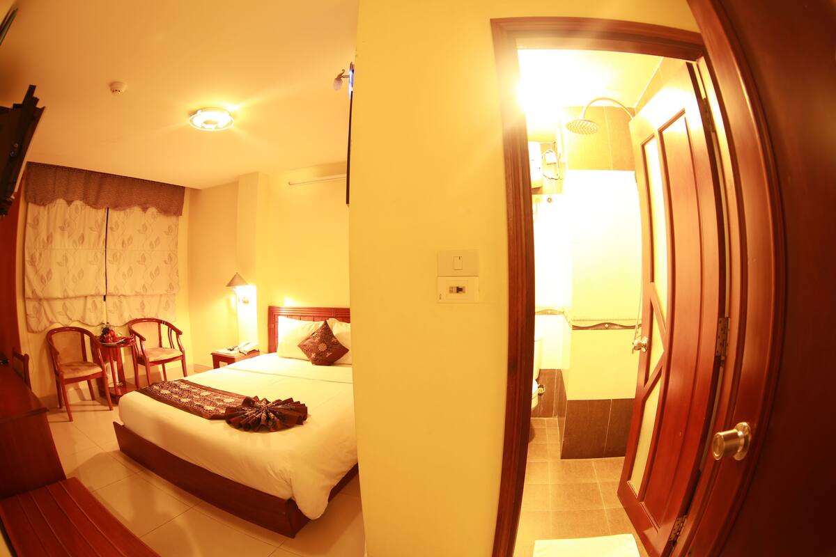 A hotel room with a bed, chairs, a desk, and a bathroom visible through an open door.