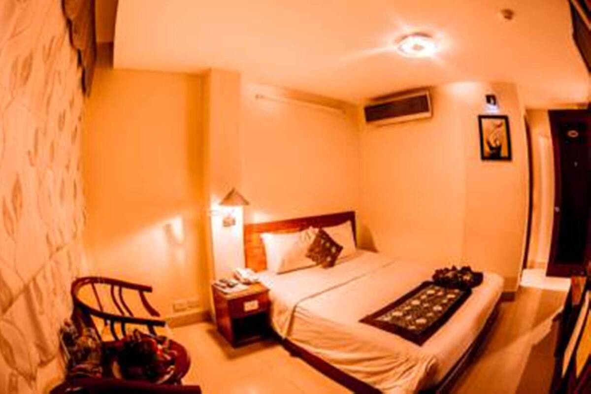 A hotel room with a bed, bedside table, lamp, and a small seating area.