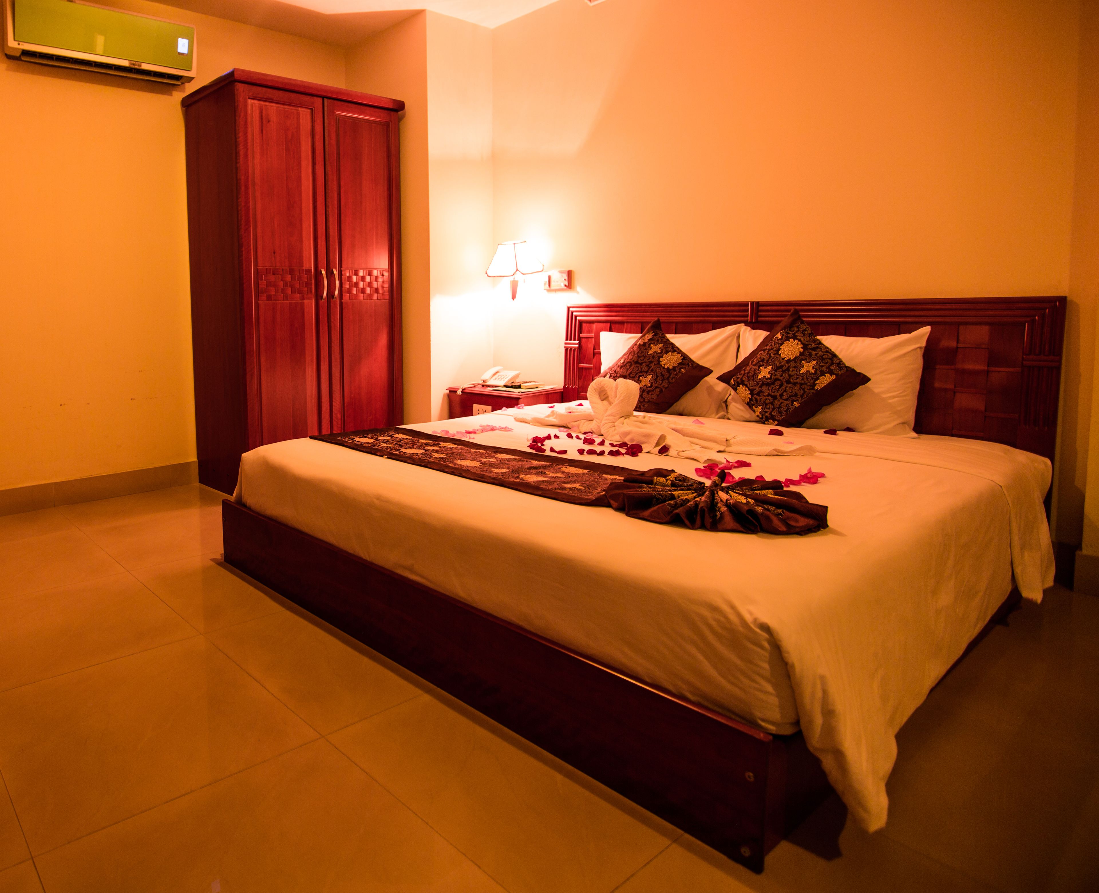 A hotel room with a large bed, wooden headboard, and a wardrobe.