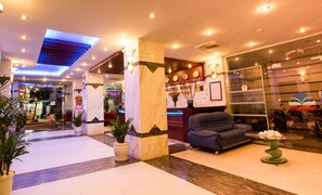 Un hall d'hôtel avec un comptoir d'accueil, un canapé, des plantes en pot et un panneau lumineux au néon.