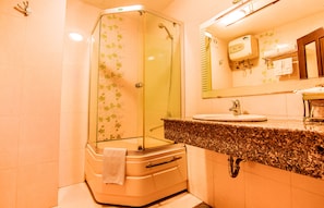 Une salle de bain avec une douche à parois de verre, un lavabo avec un miroir au-dessus et une serviette accrochée à la porte de la douche.