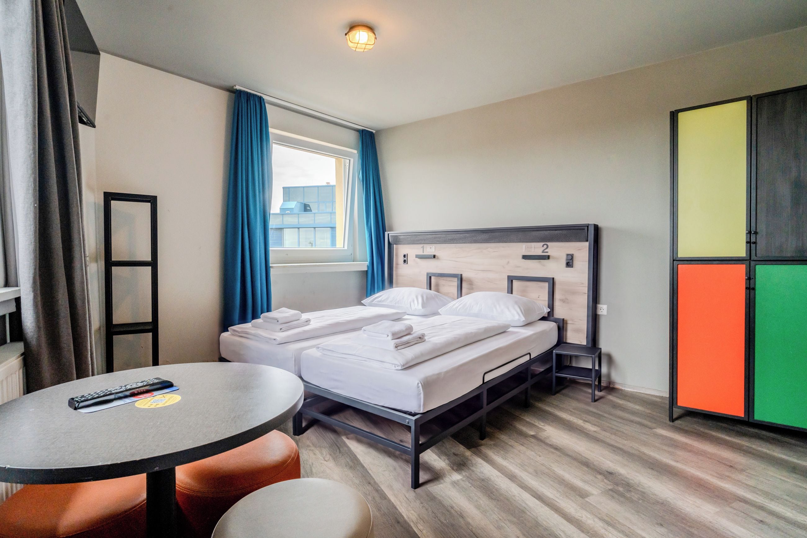 A hotel room with a bed, a table, a chair, a wardrobe, and a window with curtains.