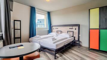 A hotel room with a bed, a table, a chair, a wardrobe, and a window with curtains.