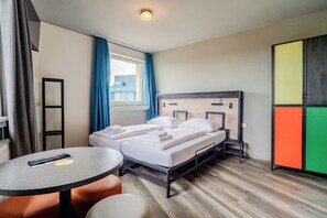Une chambre d’hôtel avec un lit, une table, une chaise, une armoire et une fenêtre avec des rideaux.