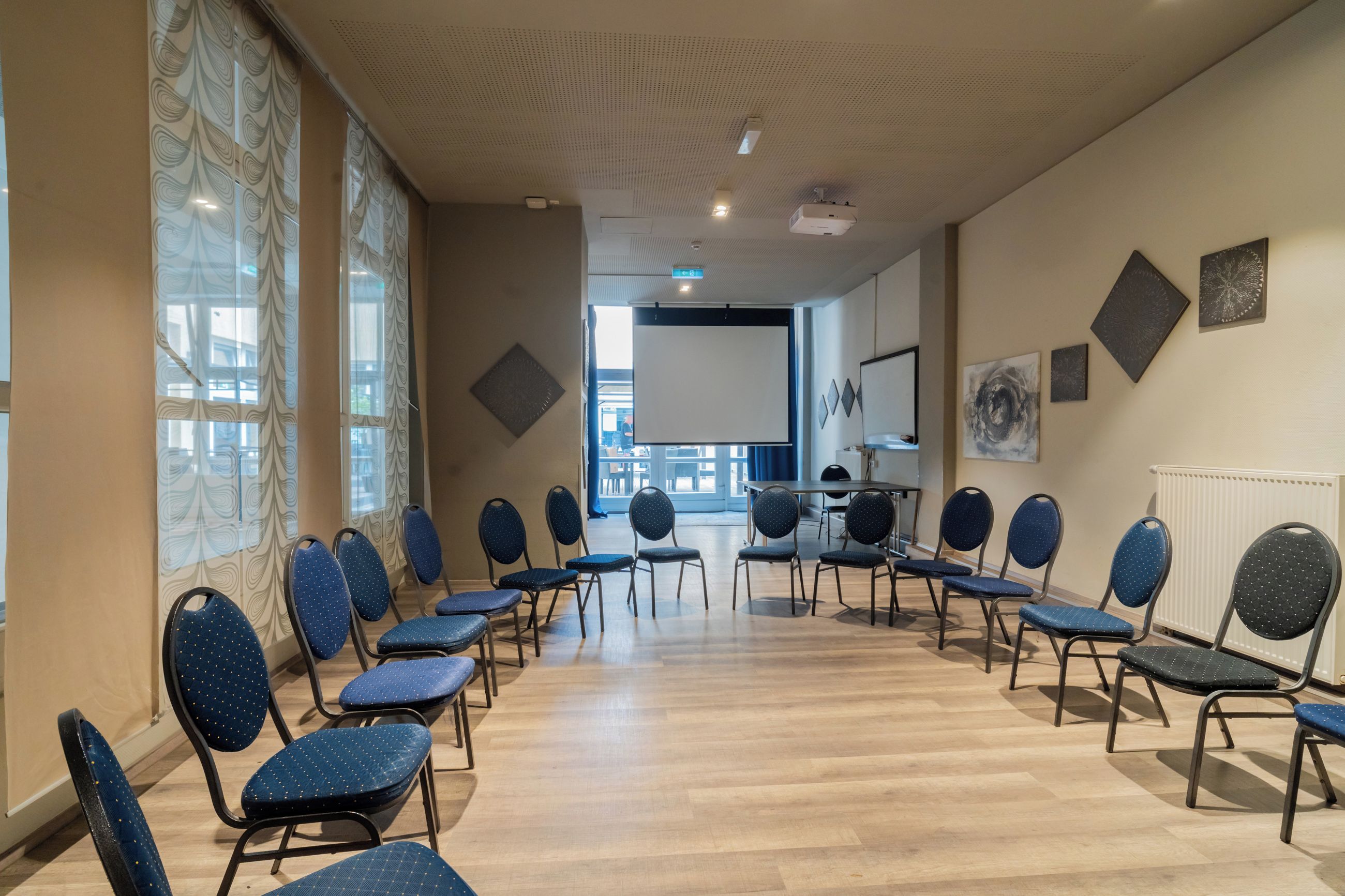 Un salón de conferencias con filas de sillas, una pantalla de proyector y una pizarra.