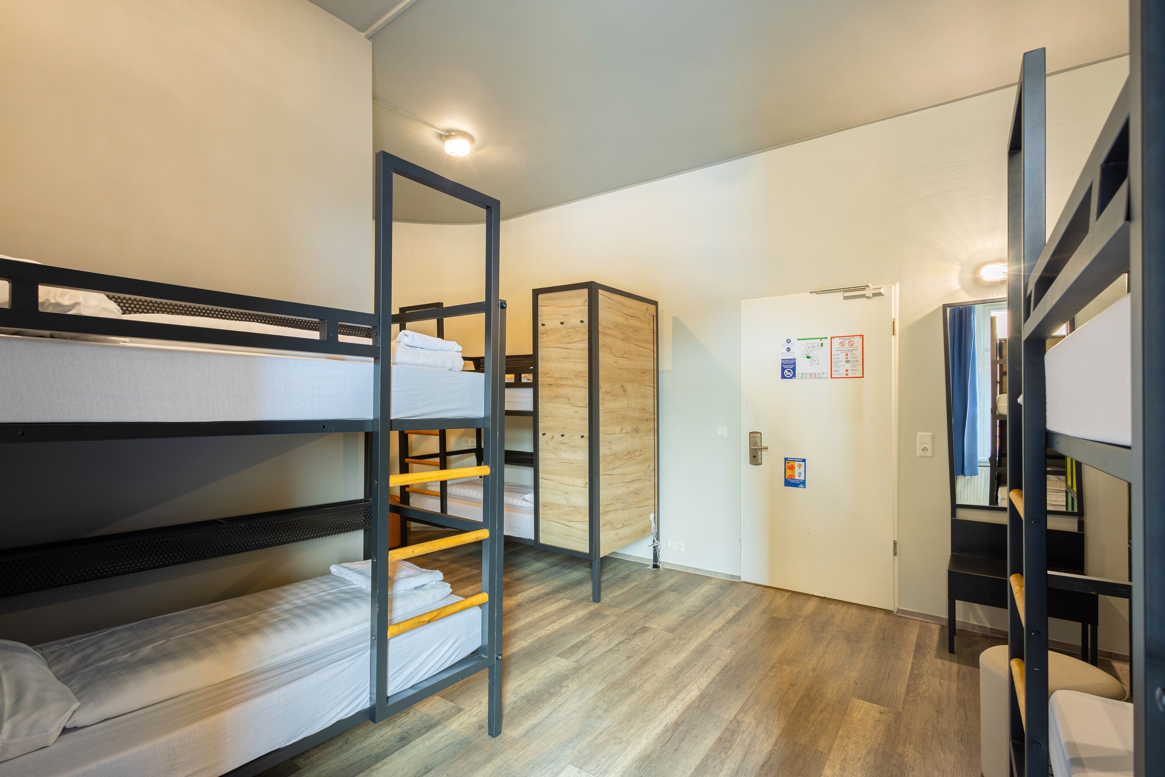 Ein Schlafsaalzimmer mit Etagenbetten, einem Holzschrank und einer Tür mit angebrachten Schildern.