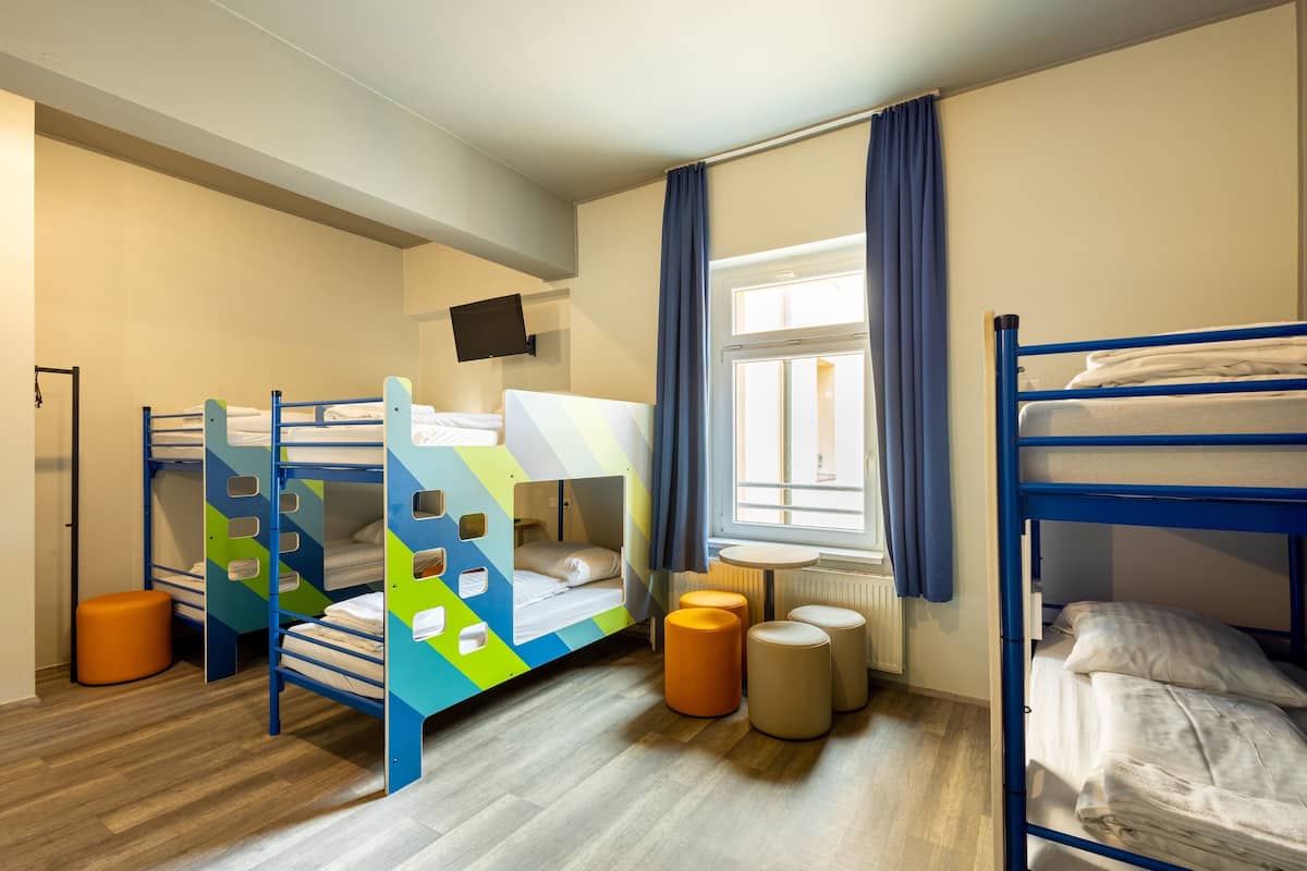Une chambre d’enfant avec des lits superposés, une télévision, une fenêtre avec des rideaux et une petite table ronde.