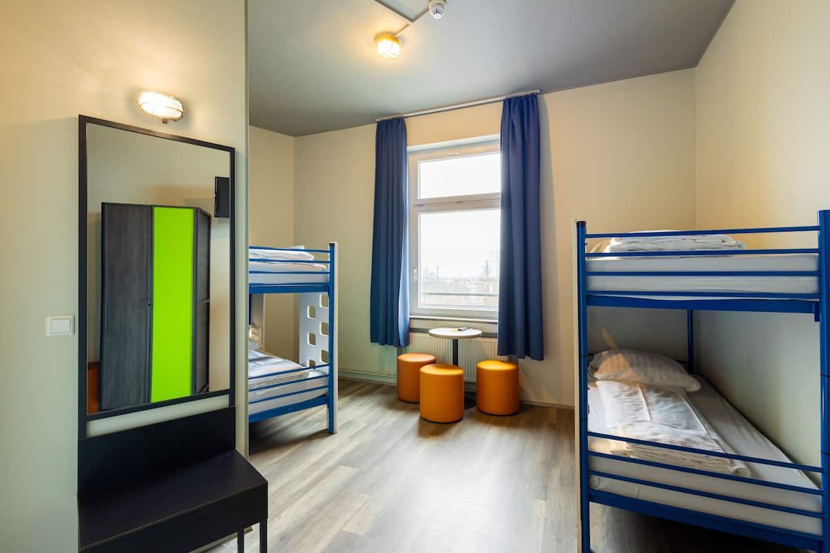 Une chambre avec des lits superposés, un miroir, une petite table et une fenêtre avec des rideaux.
