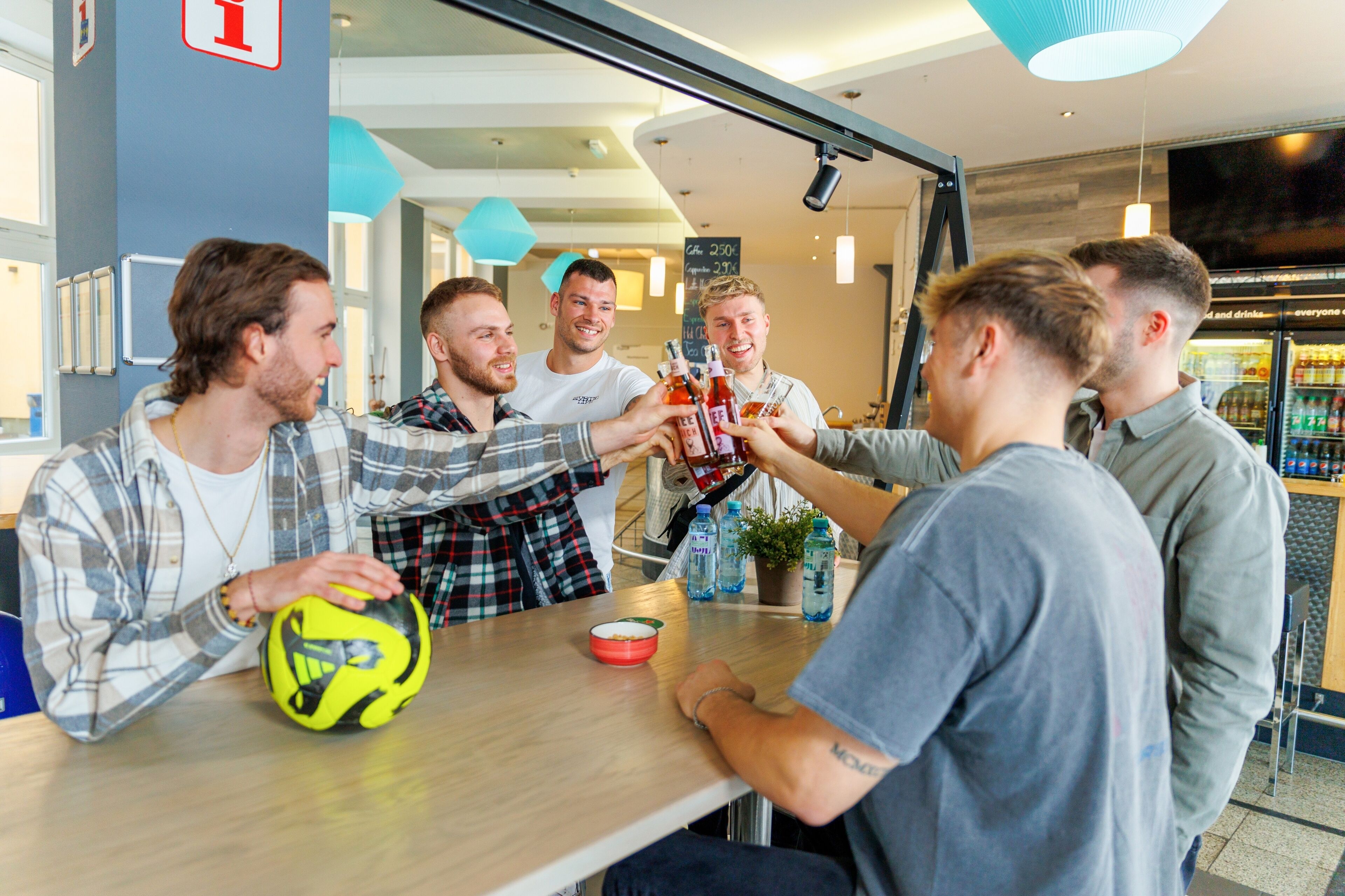 Un grupo de personas brindando con bebidas en una mesa, junto a una pelota deportiva y un tazón.