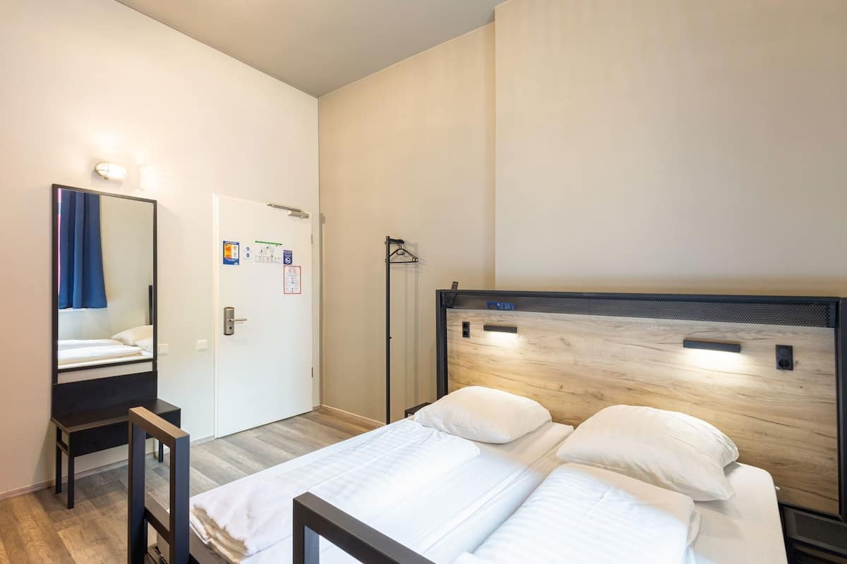 Une chambre à coucher comprenant un lit, une table de chevet, un miroir, une porte et un luminaire fixé au mur.